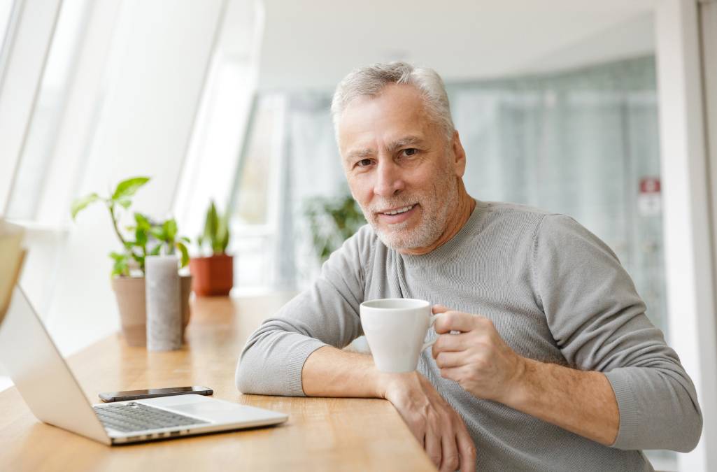 Older man drinking coffee at his computer