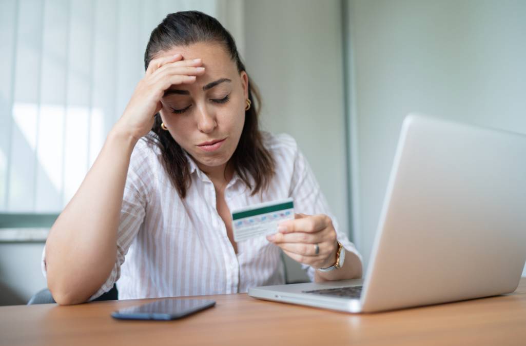 Stressed woman sitting at computer looking at credit card 